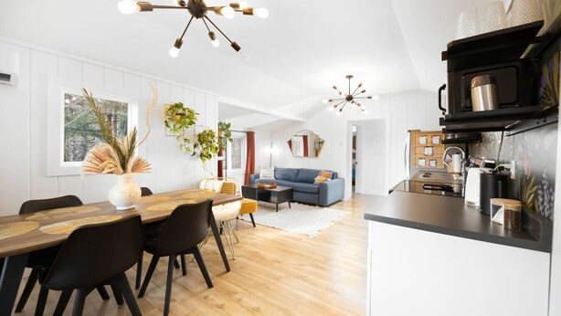 A modern kitchen with a central island, a dining area with a wooden table and chairs, and a living room with a sofa and a coffee table. - Forest cottage on the lake ☀️ (Fairfield)