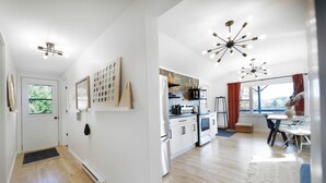A modern kitchen with white cabinets, a stove, and a dining area with a table and chairs. - Forest cottage on the lake ☀️ (Fairfield)