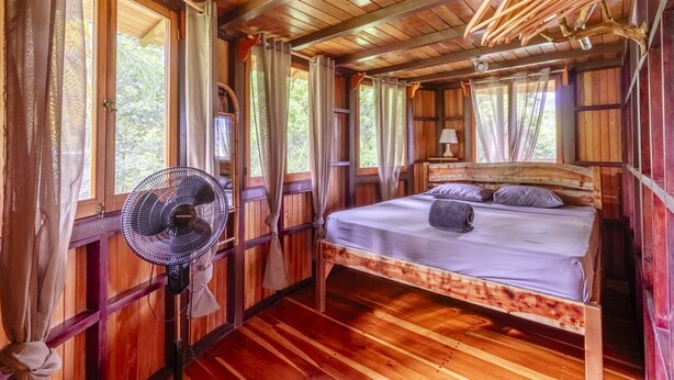 A wooden cabin room with a bed, a fan, and curtains. - Paradiselodge - Jungleguesthouse - next to Nauyaca (Platanillo de Baru)