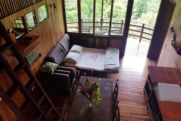 Un intérieur en bois avec un canapé, une table à manger et des chaises, et une vue dégagée grâce à de grandes fenêtres.