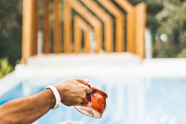 Una mano vertiendo líquido de un vaso a una taza cerca de una piscina.