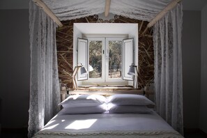 Ein Bett mit Baldachin, ein Fenster mit Blick auf Bäume und zwei Nachttischlampen.