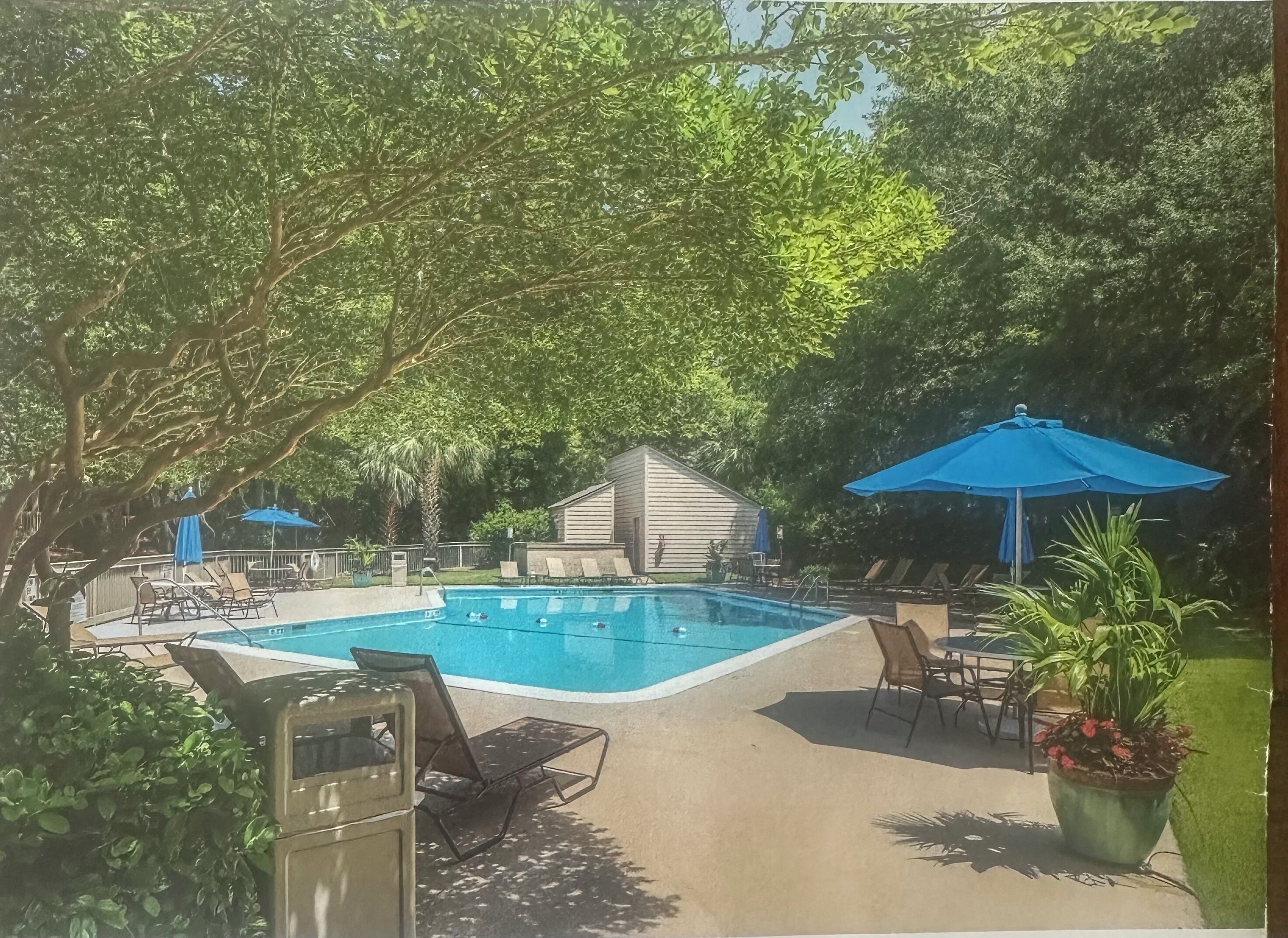 Ein Swimmingpool, umgeben von Liegestühlen und Sonnenschirmen, mit einem kleinen Gebäude im Hintergrund.