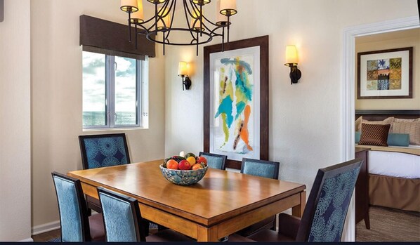 A dining area with a wooden table, chairs, a fruit bowl, and a chandelier.