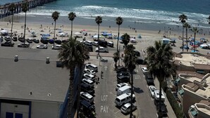 A beach view with a parking lot, beach umbrellas, and a pier in the background. - Presidential Suite - 4-bedroom awesome hotel suite in fabulous Oceanside (Oceanside)