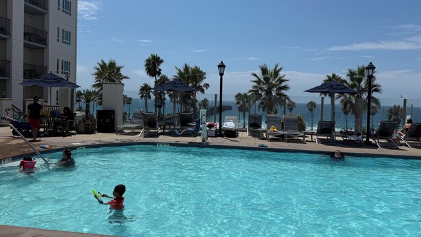 A pool area with lounge chairs and umbrellas, a view of the ocean, and a building with balconies. - Presidential Suite - 4-bedroom awesome hotel suite in fabulous Oceanside (Oceanside)