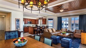 A spacious living room with a wooden dining table, blue upholstered chairs, and a fruit bowl. There is a kitchen area with wooden cabinets and a ceiling fan. - Presidential Suite - 4-bedroom awesome hotel suite in fabulous Oceanside (Oceanside)