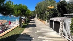 Un sendero pavimentado con diseño a rayas, bordeado de vegetación y un edificio a un lado.