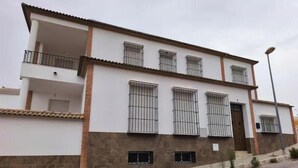 Ein zweigeschossiges Gebäude mit einem Balkon im ersten Stock, zahlreichen Fenstern mit Metallgitter und einer kleinen Eingangstür.