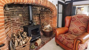 A cozy room with a brick fireplace, a leather armchair, and a basket of firewood. - The Old House (Southampton)
