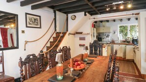 A dining area with a wooden table set for four, a staircase, and a kitchen in the background. - The Old House (Southampton)