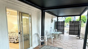 A covered patio area with a sliding glass door leading to a bedroom, a table with chairs, and a patterned floor. - 2 Private Acres - 2 Houses - 5 Bed Rooms 4 Bath - 2 Kitchens - Single Level  (Hillsboro)