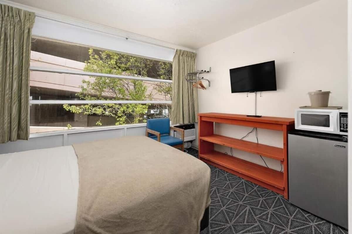 A hotel room with a bed, a desk with a microwave, a television, and a window with curtains.