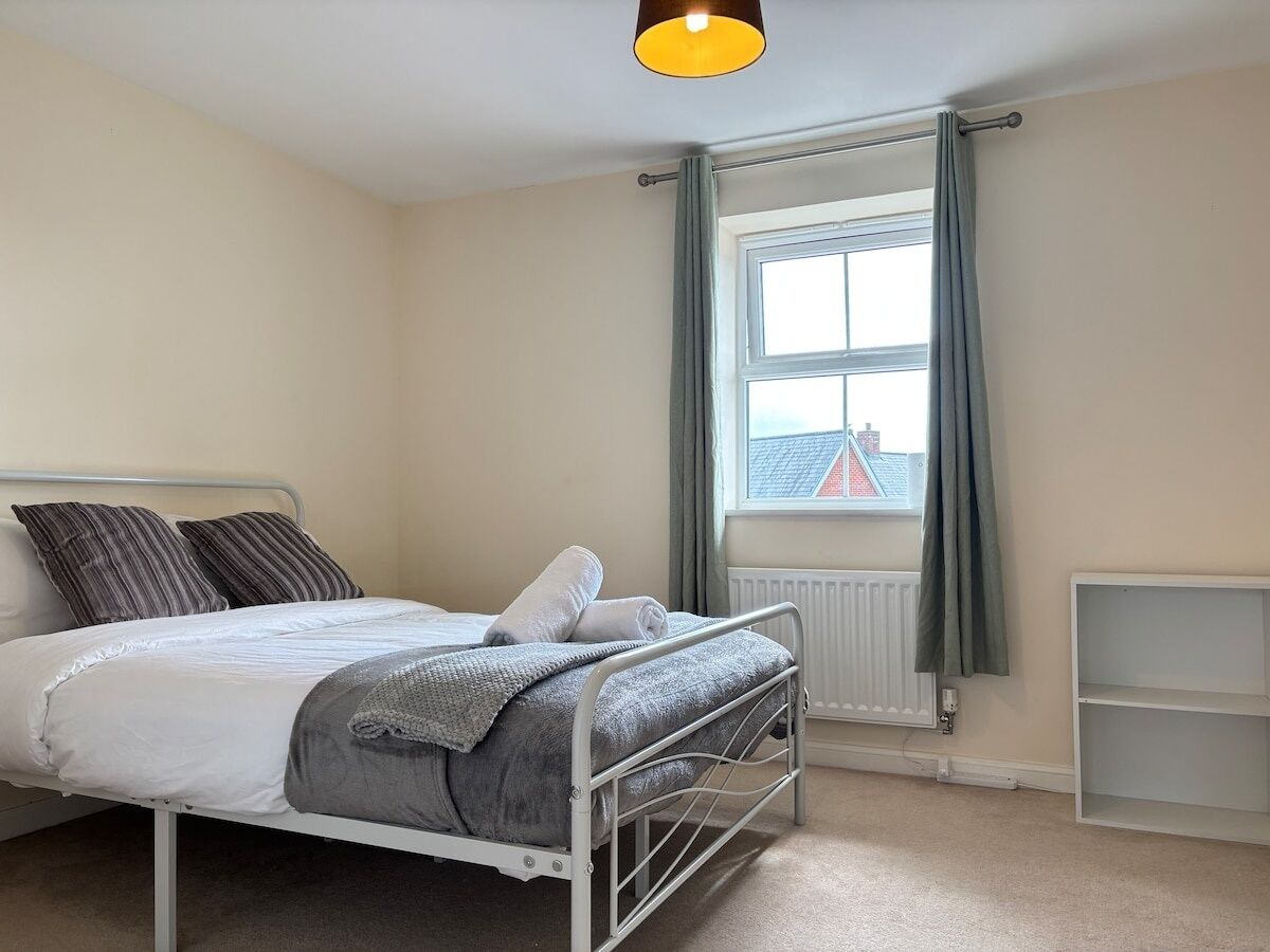 Une chambre à coucher avec un lit, un radiateur, une fenêtre avec des rideaux et une étagère.