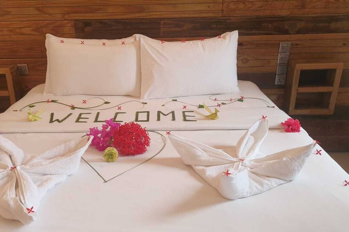 A neatly made bed with a 'WELCOME' sign, towels, and decorative flowers.