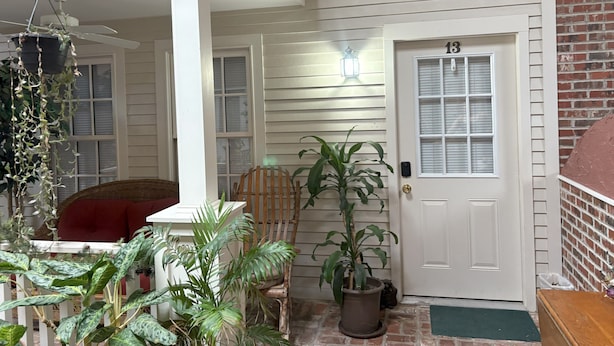 A porch with a white door marked '13', a wooden chair, a potted plant, and a hanging plant with vines. - 2-bedroom apartment in wonderful Lorain with AC (Lorain)