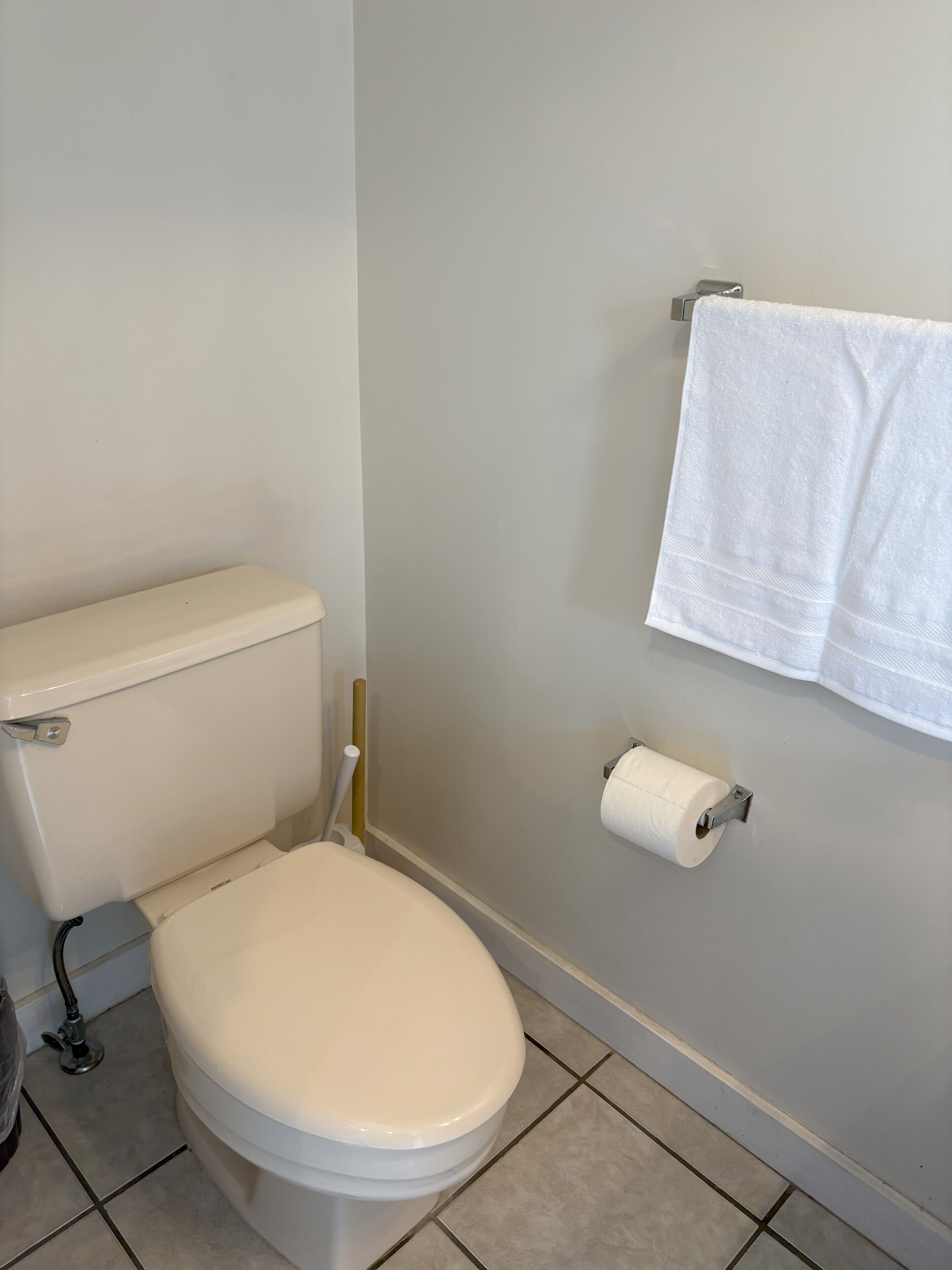A toilet with a white seat and tank, a toilet paper holder, and a towel hanging on a rack.