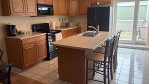 A kitchen with wooden cabinets, a black refrigerator, a microwave, a stove, and a sink. There is a bar stool and a chair near the sink. - 2-bedroom apartment in wonderful Lorain with AC (Lorain)