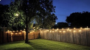 A backyard with a wooden fence, string lights, and a tree. - Entire Spacious and beautiful 5 Bedroom House (Garland)