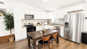 A modern kitchen with white cabinets, stainless steel appliances, a wooden dining table, and chairs. - Entire Spacious and beautiful 5 Bedroom House (Garland)