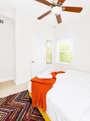 A bedroom with a bed, a ceiling fan, a door, and a window.