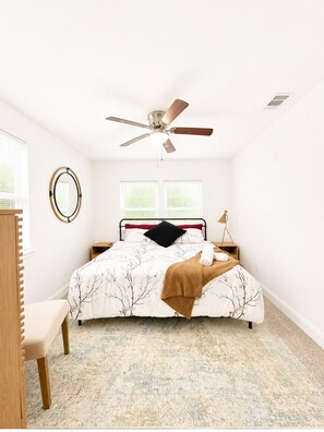 Une chambre à coucher avec un lit, un ventilateur de plafond, une table de chevet, une chaise et une fenêtre.