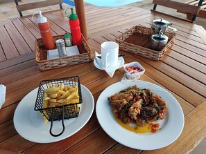 Una mesa de madera con una cesta que contiene condimentos, una porción de papas fritas, una taza y otra cesta con una olla.