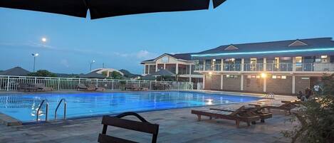 A swimming pool with lounge chairs and umbrellas, a building with a sign reading "Resort", and a clear sky.