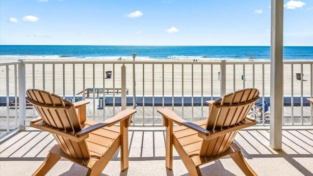 Ein Balkon mit zwei Holzsesseln und einem Tisch, mit Blick auf einen Strand und freier Sicht auf das Meer und den Sandstrand.