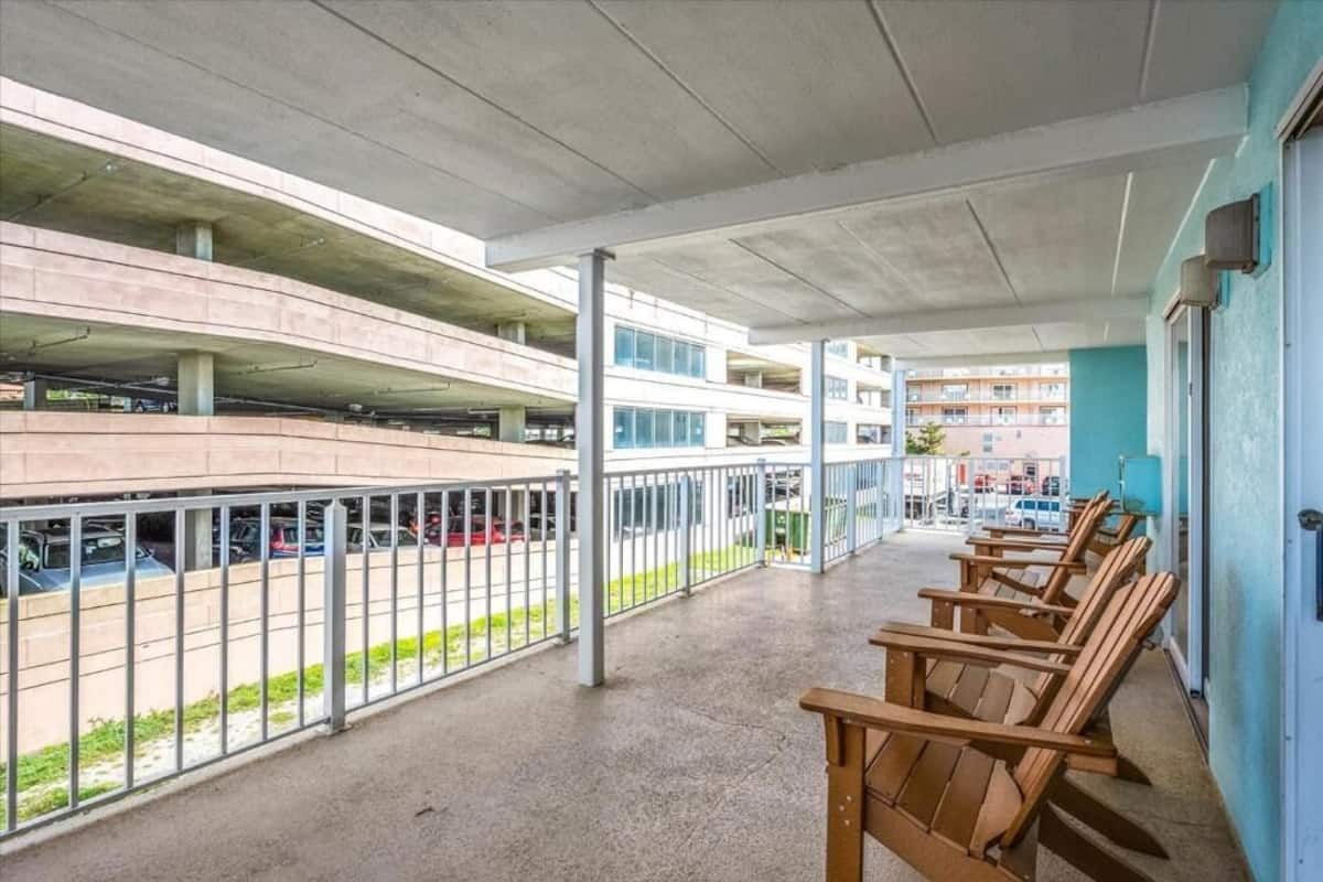 A covered outdoor area with a concrete floor, metal railings, and wooden chairs.