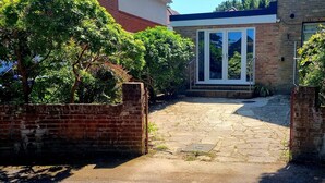 A paved driveway leading to a house with a brick wall and a small window.