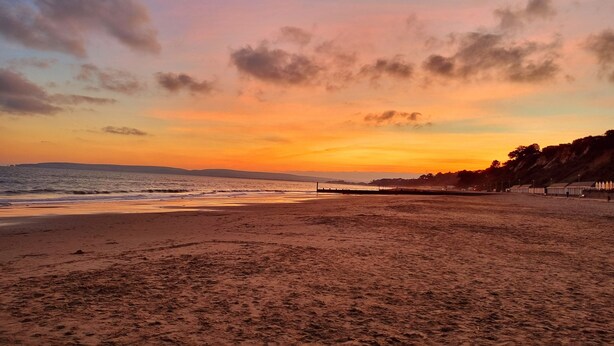 A beach with a sunset, sandy shore, and distant hills.