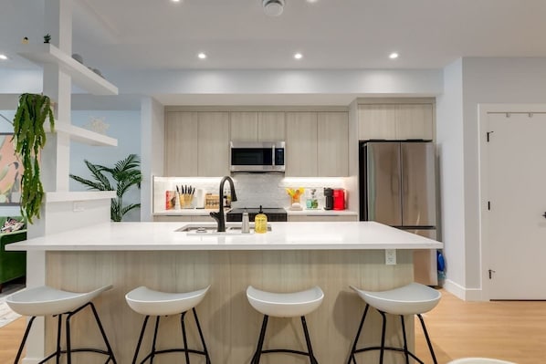 A modern kitchen with a central island, bar stools, stainless steel appliances, and light wood cabinetry.