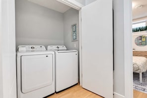 A laundry room with two white Samsung washing machines, a door leading to another room, and a framed picture on the wall.