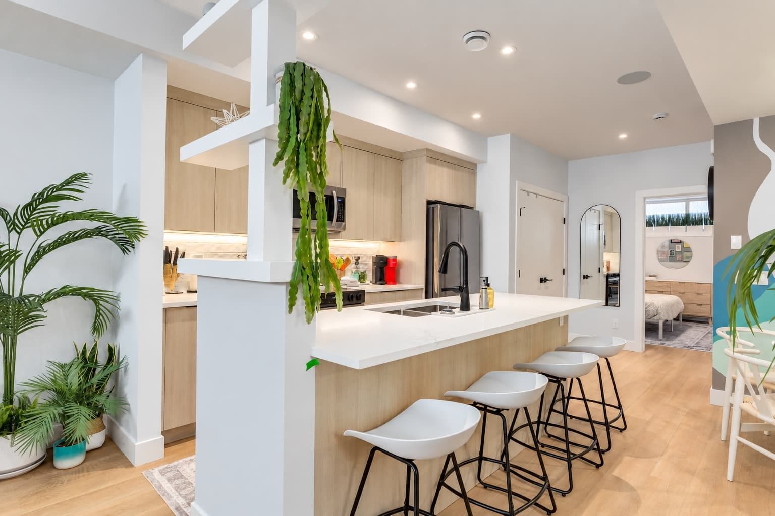 A modern kitchen with a central island, bar stools, and a hanging plant.