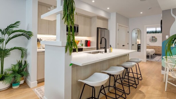 A modern kitchen with a central island, bar stools, and potted plants. - 1BR/1BA Apartment | King Casper Bed | Sleeps 4 (Calgary)