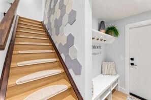 A staircase with wooden steps and woven mats, a wall with hexagonal tiles, a white console table, and a door labeled 'DROOM'. - Kensington Art Suite | King Bed & Private Entry (Calgary)