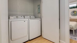 Ein Waschraum mit zwei weißen Waschmaschinen und einer Tür zu einem Schlafzimmer.