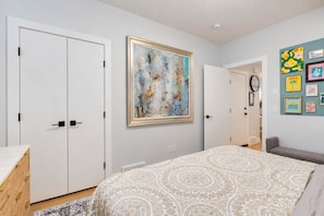 A bedroom with a bed, a wardrobe, a painting, and a wall with framed pictures.