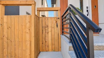 A wooden gate leading to a building with a metal staircase and a door with a keypad.