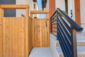 A wooden gate leading to a building with a metal staircase and a door with a keypad. - Kensington Art Suite | King Bed & Private Entry (Calgary)