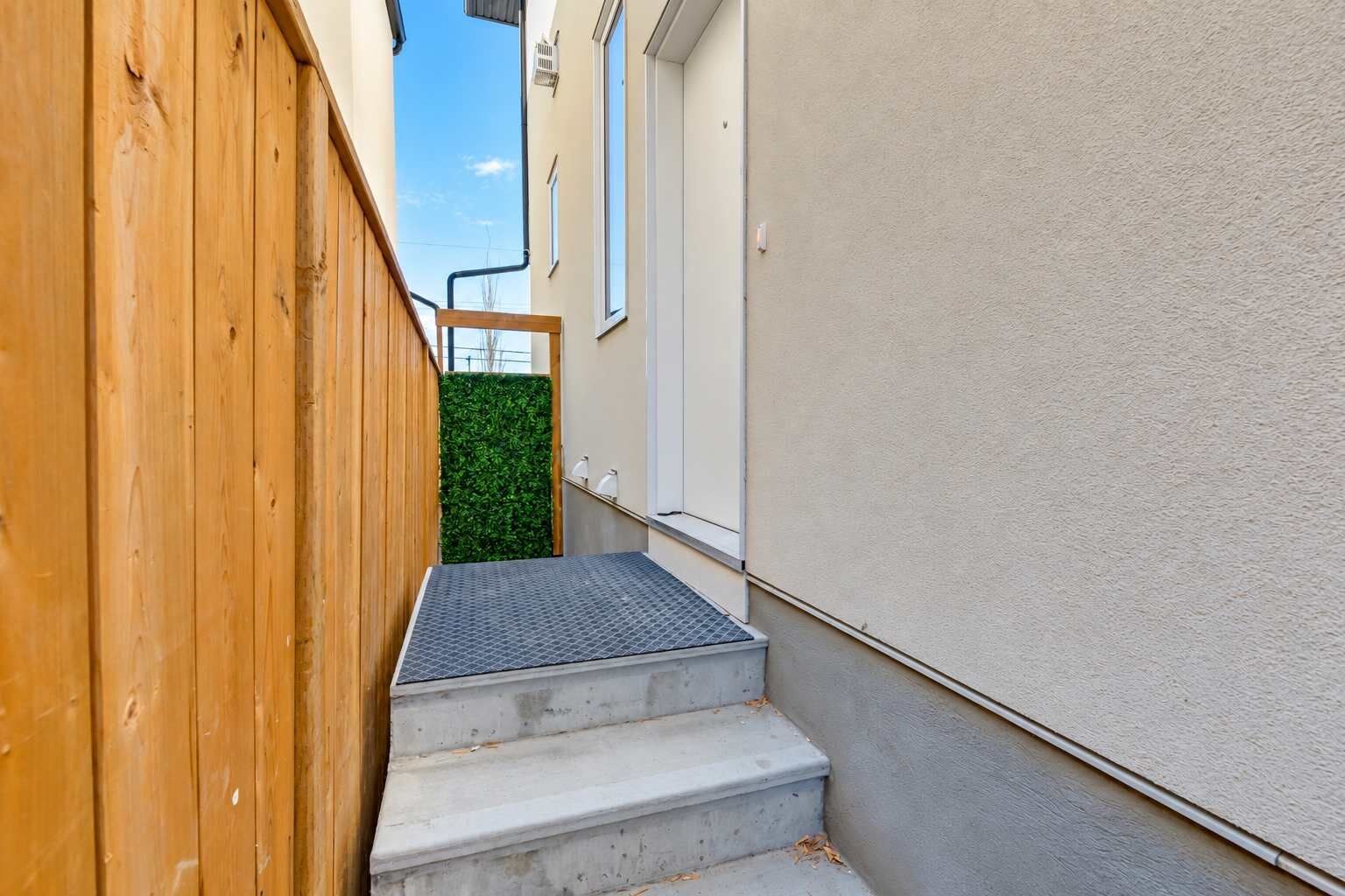 A narrow outdoor corridor with a wooden fence on one side and a white wall on the other.