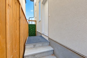 A narrow outdoor corridor with a wooden fence on one side and a white wall on the other.