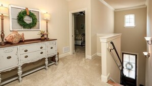 Un couloir avec une commode blanche, une guirlande accrochée au mur et un escalier.