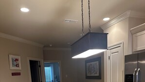 Une cuisine dotée d’un comptoir en granit, d’un réfrigérateur en acier inoxydable et d’un luminaire suspendu. On y trouve deux tabourets et un meuble contenant des objets décoratifs.