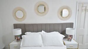 A bedroom with a bed, two bedside tables, three wall mirrors, and a door. - Enchanting 3-bedroom house in Stockport (Stockport)