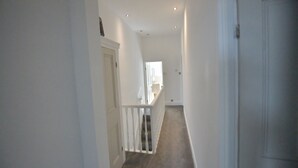 A narrow, white-walled hallway with a carpeted floor leading to a door at the end. - Enchanting 3-bedroom house in Stockport (Stockport)