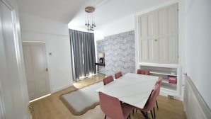 A dining area with a white table and pink chairs, a patterned wallpaper wall, and a white door. - Enchanting 3-bedroom house in Stockport (Stockport)
