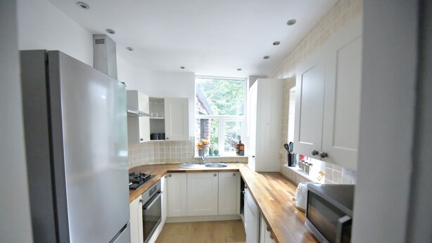 A modern kitchen with white cabinets, stainless steel appliances, and a wooden countertop. - Enchanting 3-bedroom house in Stockport (Stockport)