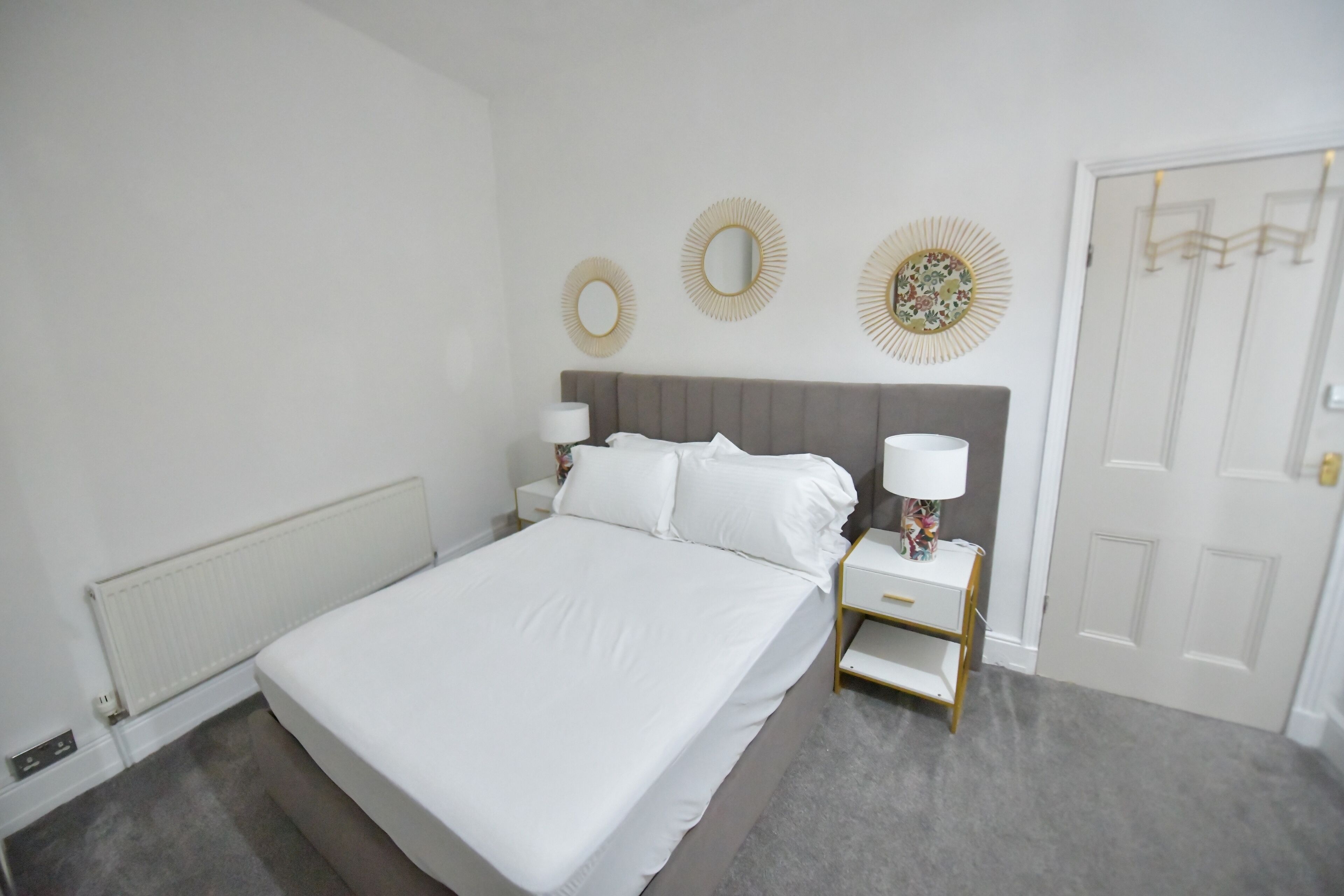 Ein ordentlich eingerichtetes Schlafzimmer mit einem Bett, Nachttischen und dekorativen Wandspiegeln.